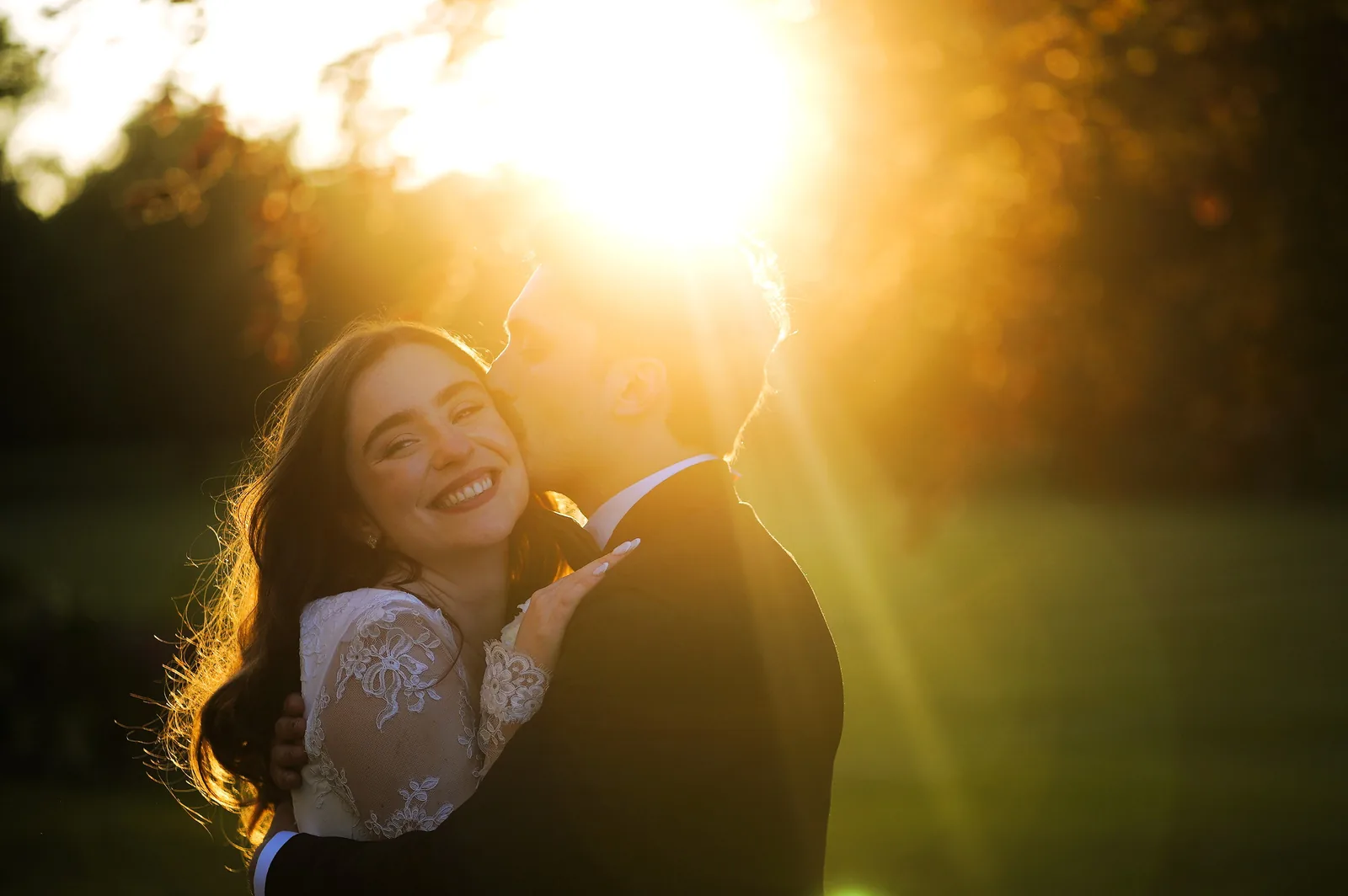 Bride and groom laughing together at golden hour with sun flare