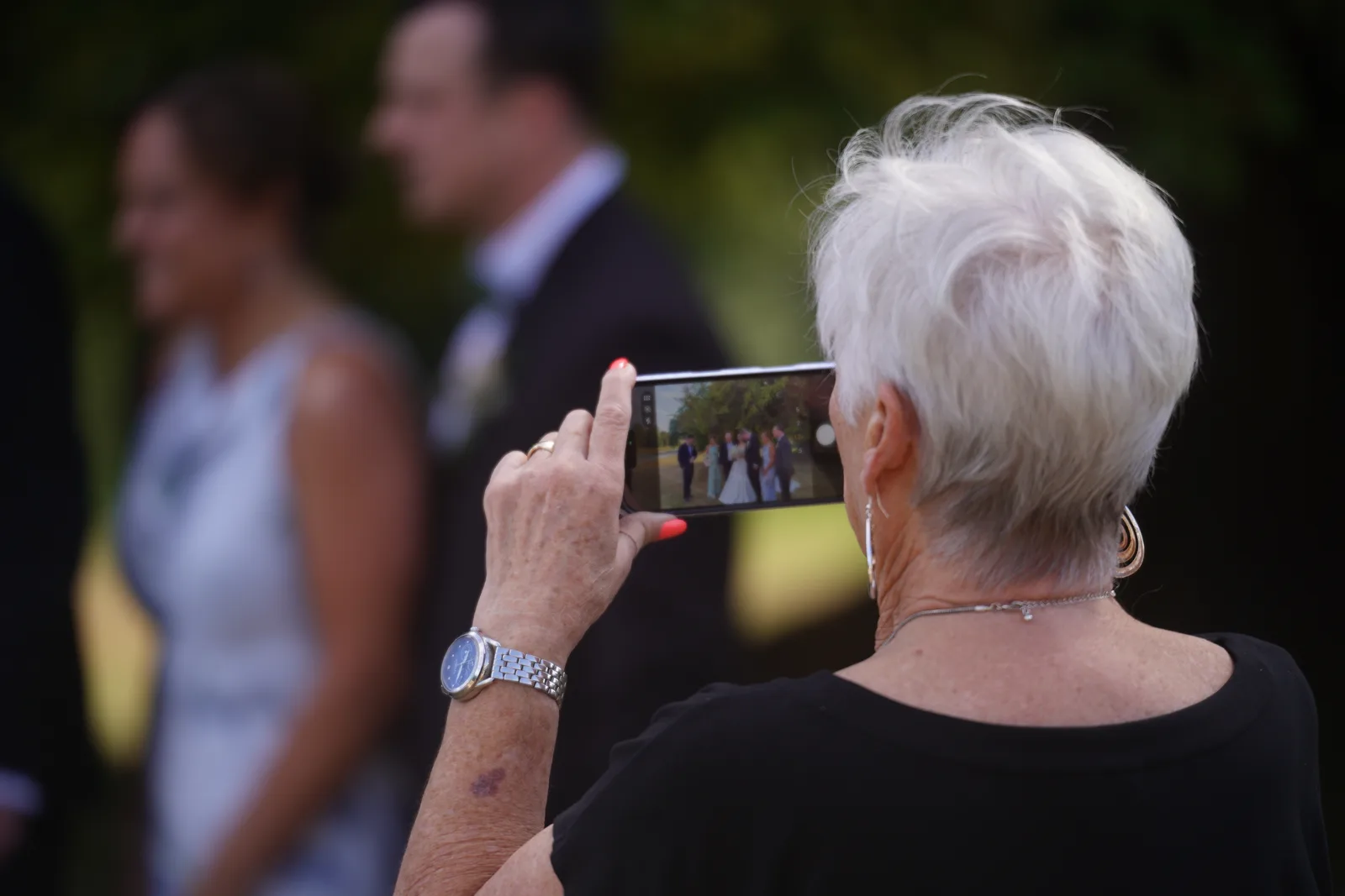 A wedding guest filming the couple on a phone, with photo and video modes visible on screen