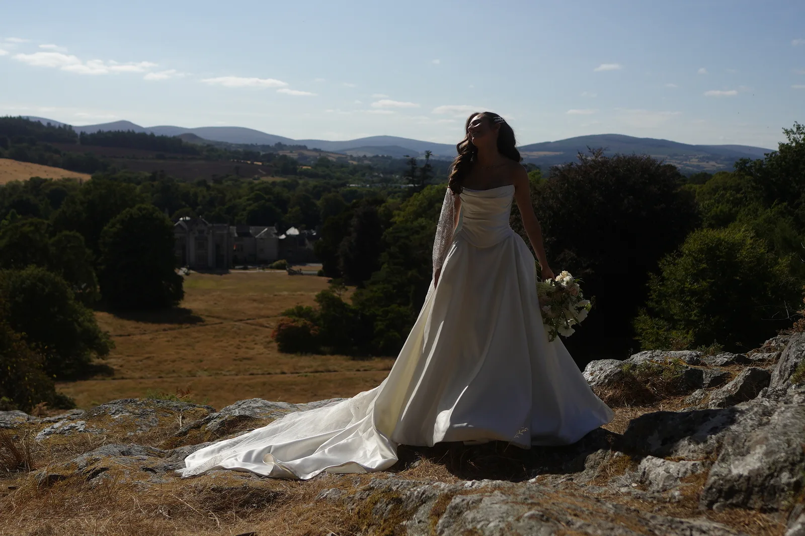 A bride standing on rocks above Killruddery with the Wicklow hills stretching out behind her