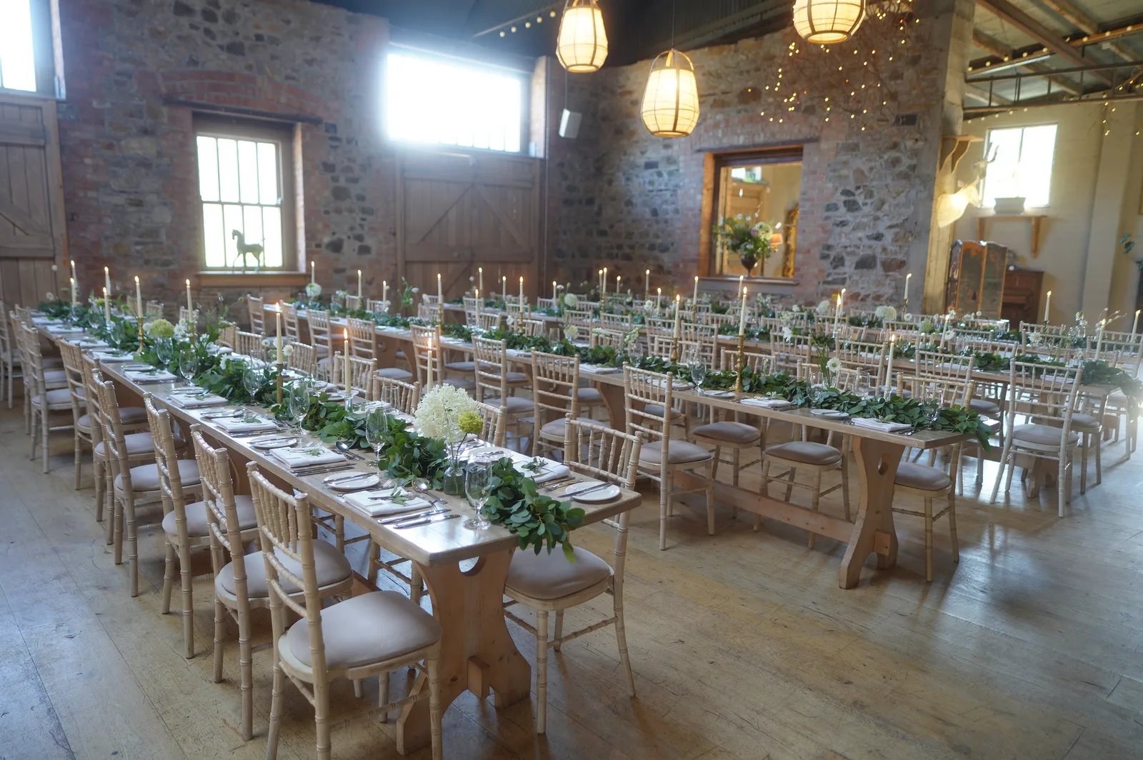 The Grain Store at Killruddery set for a wedding dinner, long timber tables with greenery and candles against stone walls