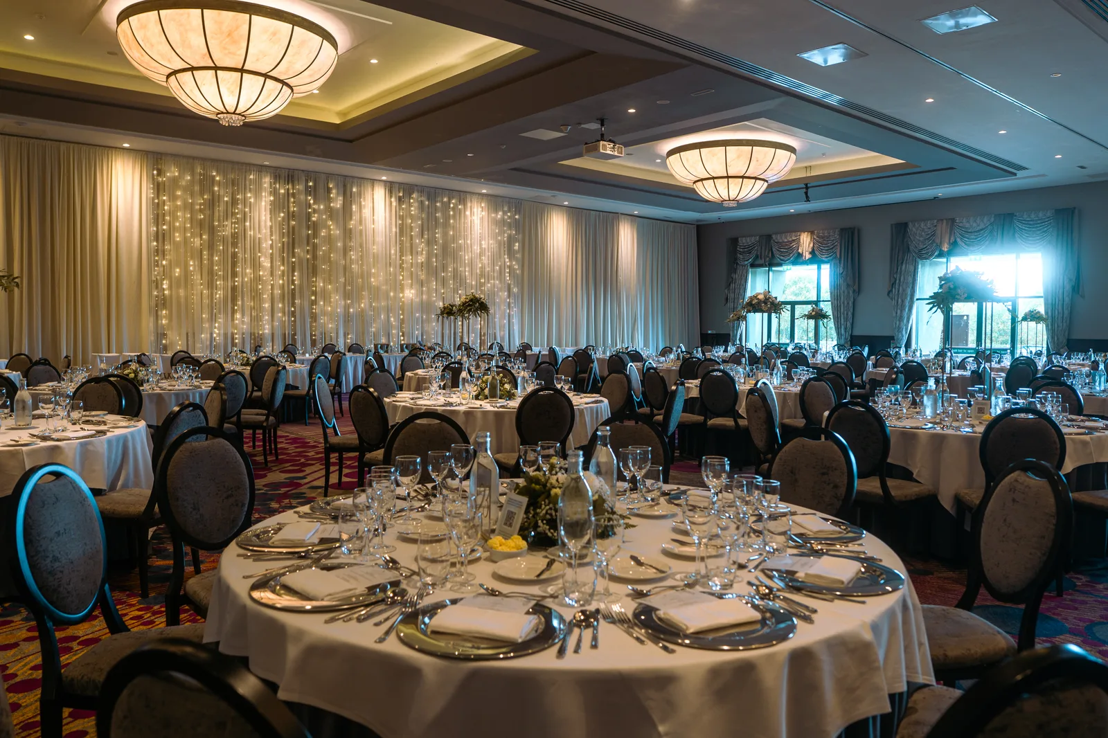 The Lyrath Estate ballroom set for a wedding dinner, round tables and a floor-to-ceiling fairy-light curtain along the back wall