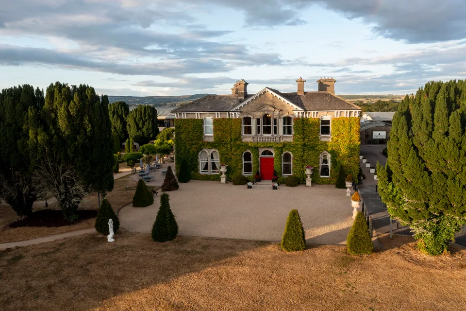 Lyrath Estate's ivy-covered original house seen from the air, with a red front door and a gravel courtyard in evening light